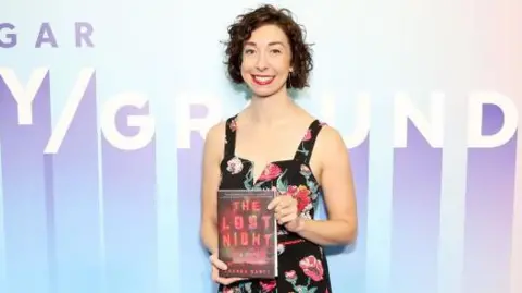 Judge backs AI firm over use of copyrighted books - Judge backs AI firm over use of copyrighted books.webp Getty Images Author Andrea Bartz at an event holding a hardback copy of her novel The Lost Night. She is wearing a black sleeveless dress with a rose pattern