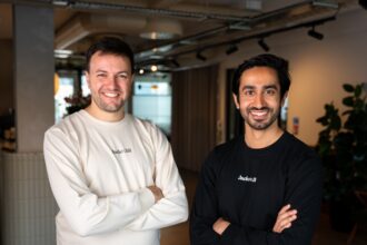 Two men stand with folded arms in a corporate office.