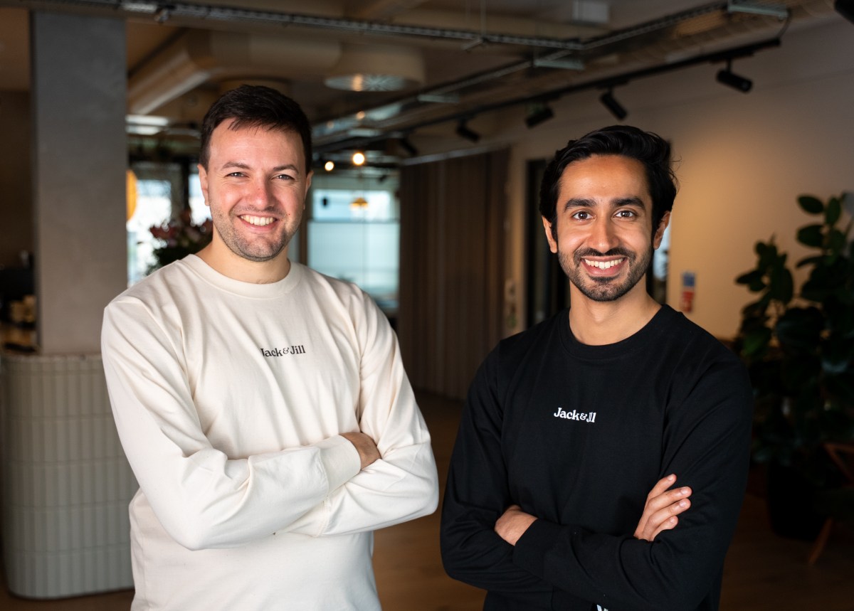 Two men stand with folded arms in a corporate office.